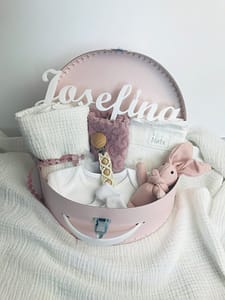 Růžový dárkový kufřík pro miminko. Obsahuje vyšívaný ručníček, mušelínovou plenku, bílé body a ponožky, zajíce a klip na dudlík